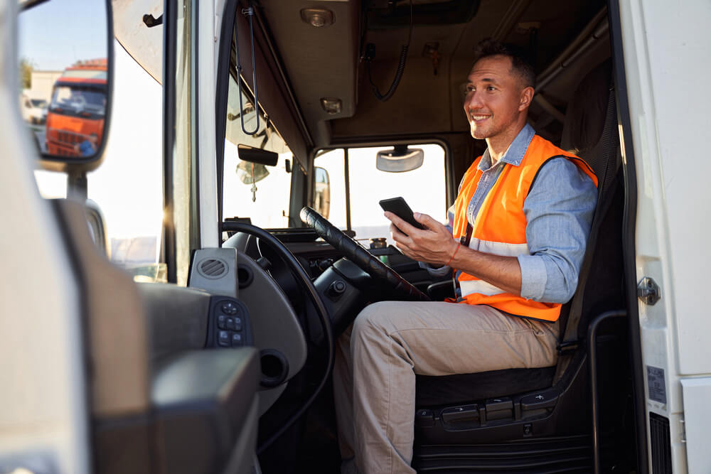 truck driver in drivers cap holding mobile phone